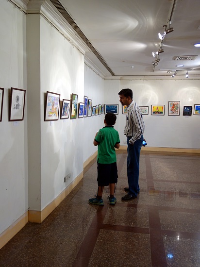 Father and son discuss a painting on display at Khula Aasmaan - Children's Art Exhibition - Edition I, presented by Indiaart Gallery