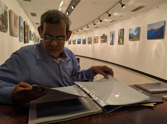 Suhas Phadke going through the catalog of the show Call of the Hills by Milind Vishwas Sathe at Jehangir Art Gallery, Mumbai