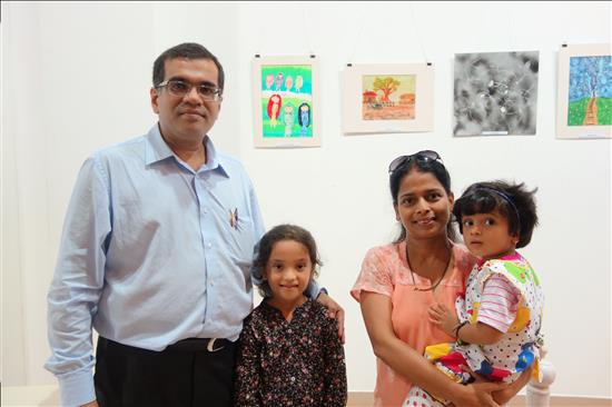 The girl standing with her painting in the background along with parents and younger sibling